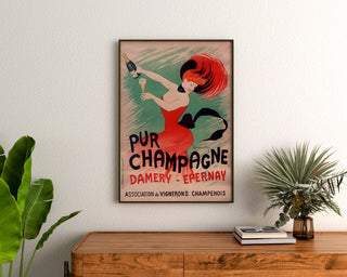 Póster publicitario vintage Champagne Damery-Épernay, enmarcado sobre una cómoda de madera, entre plantas.