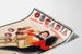Póster publicitario vintage Oscaria, calzado, presentado sobre una hoja curvada, visto en perspectiva.