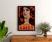 Póster publicitario vintage Perfumes Griet, enmarcado sobre una cómoda de madera, entre plantas.