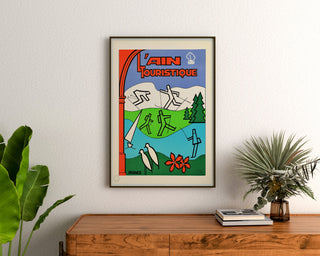 Vintage travel poster – L’Ain touristique, framed above a wooden dresser between plants.