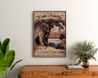 Póster vintage Aix-les-Bains, cueva de Lamartine, enmarcado sobre una cómoda de madera, entre plantas.