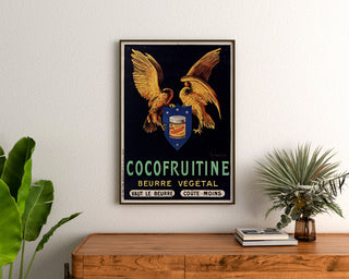 Póster vintage Cocofruitine, manteca vegetal, enmarcado sobre una cómoda de madera, entre plantas.