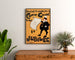 Cartel vintage Dudley Hardy, comic guide, enmarcado sobre una cómoda de madera, entre plantas.