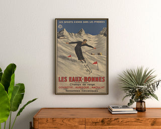 Póster vintage Les Eaux-Bonnes, deportes de invierno, enmarcado sobre una cómoda de madera, entre plantas.