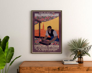 Póster vintage de Mulhouse, exposición litográfica, enmarcado sobre una cómoda de madera, entre plantas.