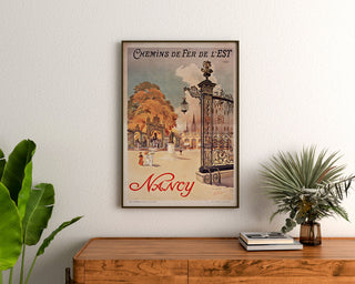 Póster vintage Nancy, chemins de fer de l’Est, enmarcado sobre una cómoda de madera, entre plantas.