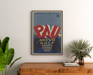Póster vintage Pau, golf y deportes, enmarcado sobre una cómoda de madera, entre plantas.