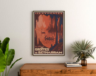 Póster vintage Pirineos, grutas de Bétharram, enmarcado sobre una cómoda de madera, entre plantas.