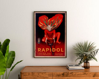 Póster vintage Rapidol, enmarcado sobre una cómoda de madera, entre plantas.